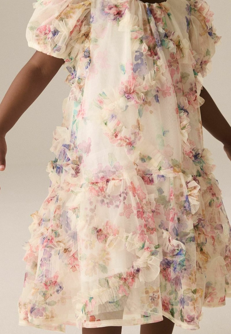 Enfant portant une robe légère et transparente avec des imprimés floraux multicolores et des détails à volants sur les manches et l'ourlet.