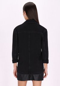 Fekete farmerdzseki laza szabással, felgöngyölt ujjak és egyenes alsó szegély. Kiemelkedő varrásokkal és egyszerű gallérral rendelkezik.