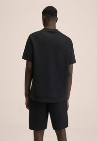 Sort atletisk sæt med en kortærmet top og matchende shorts. Stoffet ser glat ud med en afslappet pasform og raglanærmer.