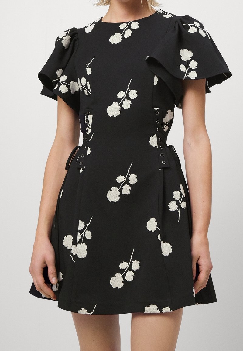 Musta mekko valkoisella kukkakirjonnalla, lyhyet röyhelösateet, tiukka vyötärö ja nyörityksellä varustetut sivut. Tasainen kangasrunko.