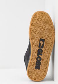 Sneaker nera con un design testurizzato e una suola in gomma naturale. Presenta un logo "GLOBE" prominente e un motivo floreale sulla suola.