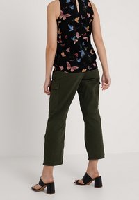 Top nero senza maniche con stampa di farfalle colorate; abbinato a pantaloni cargo verde oliva; sandali neri con tacco a blocco completano l'outfit.
