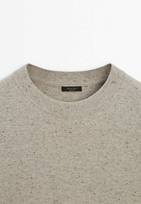 Pull gris clair à col rond, doté d'un tissu texturé avec de petites taches noires et brunes. Étiquette visible à l'intérieur du col.
