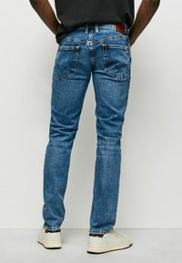 Blå denimjeans med smal passform och blekt tvätt, med två bakfickor och en brun läderlapp vid midjan.