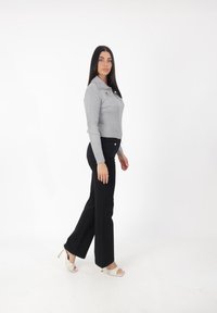 Suéter gris de canalé con cuello y bolsillos frontales, combinado con pantalones de pierna ancha negros de alta cintura y sandalias de tacón beige.