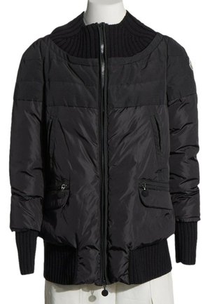 Chaqueta acolchada negra con cremallera frontal, cuello alto acanalado y puños, dos bolsillos delanteros con cremallera, mostrada en un torso de maniquí blanco.