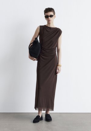 Braunes, drapiertes Midi-Kleid mit kurzen Ärmeln, kombiniert mit einer schwarzen strukturierten Handtasche und schwarzen Slippern, vor einem weißen Hintergrund.