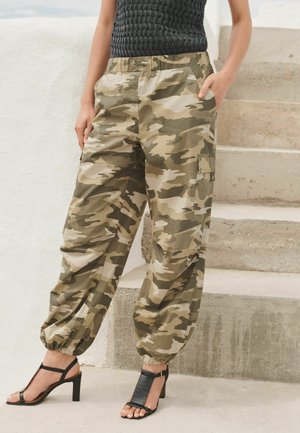 Pantalones cargo de camuflaje en tonos tierra con puños elásticos en los tobillos, bolsillos laterales y ajuste holgado, combinados con tacones negros de tiras.