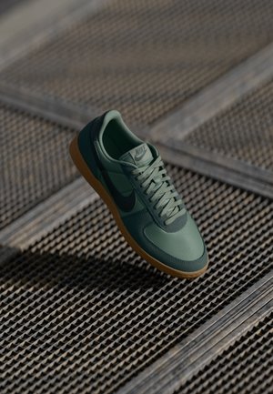Green Nike sneaker with a textured upper, contrasting dark green accents, and a gum rubber sole. Laces in matching color complete the design.