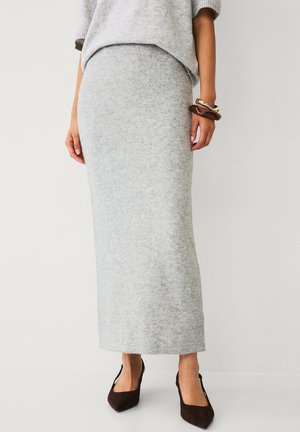 Grijze gebreide maxi-skirt met een nauwsluitende pasvorm, zachte textuur en geribde tailleband, gecombineerd met bruine hoge hakken en een lichtgrijs topje.