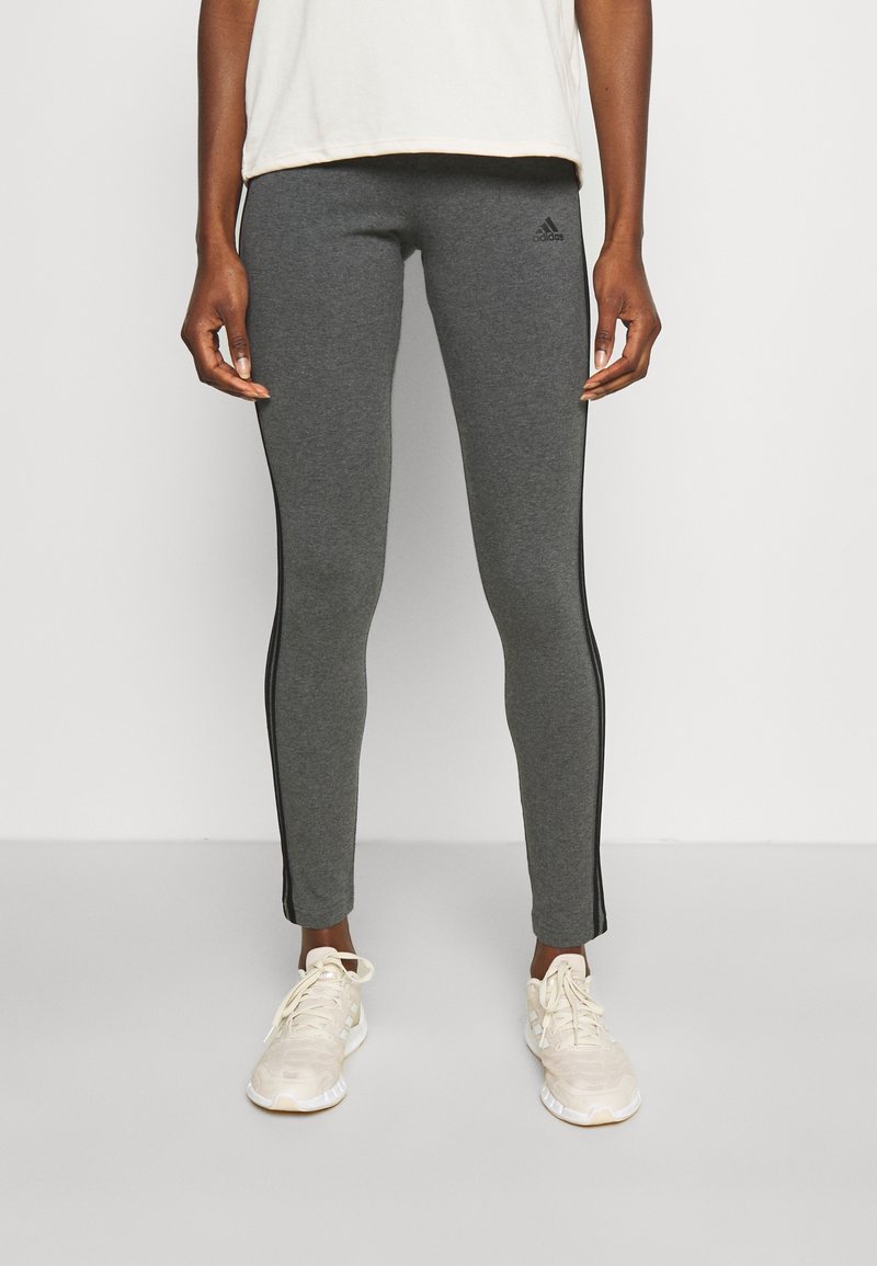 Grå leggings i en stretchig tyg med svarta sidostråk, kombinerat med en ljus topp och neutrala sneakers, med en åtsittande design.
