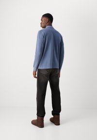 Chemise bleu à manches longues pour homme avec col, associée à un pantalon foncé et des bottines marron. Tissu lisse, coupe décontractée, design simple.