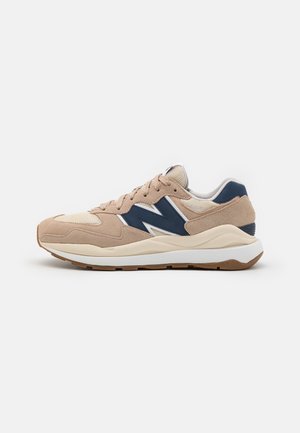 Baskets de sport beige et bleu marine avec design à lacets, tige en mesh et en daim, et semelle blanche amortie.