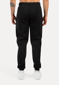 Schwarze Jogginghosen aus weichem Stoff, mit einem elastischen Bund und schmal zulaufenden Beinen. Getragen mit weißen Turnschuhen.