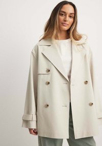 Smėlinis dvigubos krūtinės švarkas su dideliais mygtukais, plačiais atvartais ir laisvu siluetu. Pagamintas iš lygaus audinio, su pasukamomis rankovėmis ir šoninėmis kišenėmis.