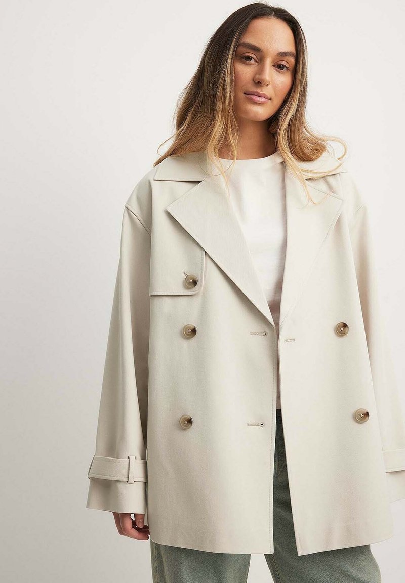 Smėlinis dvigubos krūtinės švarkas su dideliais mygtukais, plačiais atvartais ir laisvu siluetu. Pagamintas iš lygaus audinio, su pasukamomis rankovėmis ir šoninėmis kišenėmis.