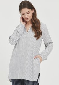 Camicia tunica leggera a righe in grigio e bianco, con scollo a V, maniche lunghe, tasche laterali e orlo leggermente curvo.
