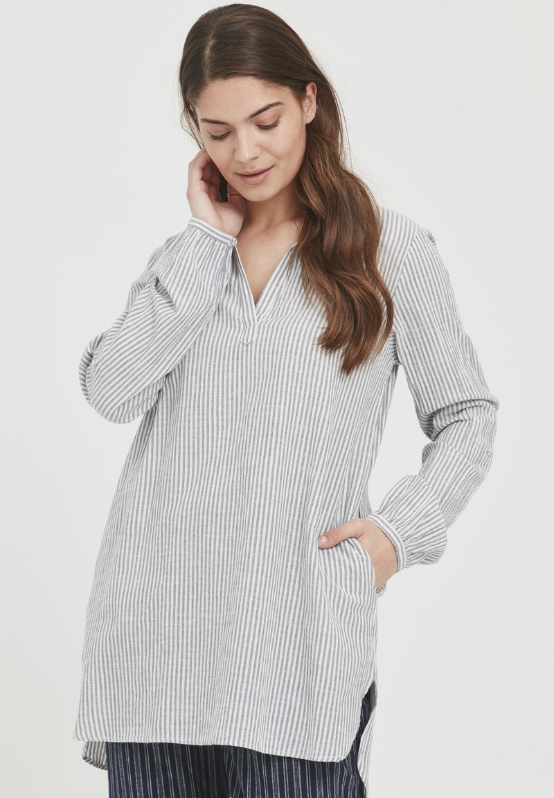Camicia tunica leggera a righe in grigio e bianco, con scollo a V, maniche lunghe, tasche laterali e orlo leggermente curvo.