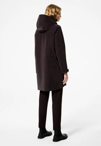 Impermeabile scuro con cappuccio, dal design elegante e aerodinamico. Realizzato in materiale impermeabile, abbinato a pantaloni neri e stivali. Texture liscia.