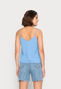 Camisola azul clara com tiras finas ajustáveis, design em V flat, combinada com calções de ganga desgastados. Textura suave, ajuste casual.