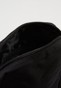 Pochetto di tessuto nero con una superficie liscia, chiusura a zip visibile e apertura superiore che rivela un interno scuro. Design semplice, uso pratico.