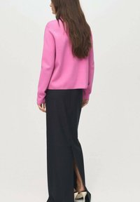 Fuchsia Pullover mit lockerer Passform, kombiniert mit einem bodenlangen schwarzen Rock mit einem seitlichen Schlitz und neutralfarbigen High Heels.