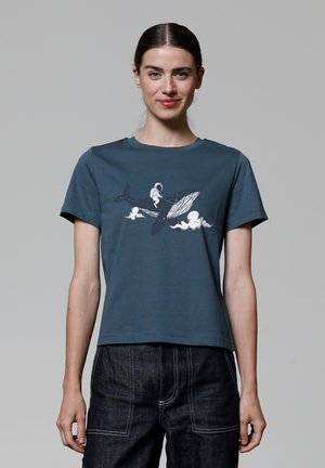 T-shirt à manches courtes teal en coton avec un graphique blanc représentant une baleine et un astronaute sur fond de nuages. Encolure ronde, coupe décontractée.
