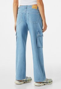 Ljusblå denim cargo-byxor med vida ben, utrustade med sidofickor och en brun märkesetikett på midjan. Mjuk textur och avslappnad design.