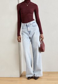 Haut col roulé côtelé bordeaux, jean jean large bleu clair, talons pointus marron et sac bandoulière grenat. Textures lisses et coupe décontractée.