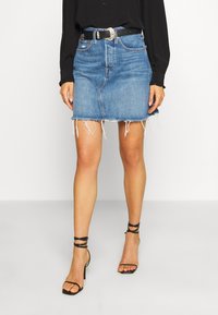 Jeansminikjol med fransad nederkant, ljusblå färg, fem fickor och ett svart bälte med en silverspänne, tillsammans med svarta sandaletter med remmar.