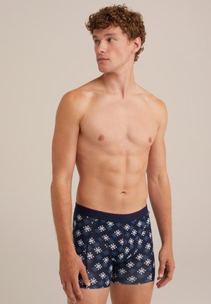 Herreboxershorts med en marineblå bund prydet med et hvidt snefnugmønster. Fremstillet af blødt stof med en kontrasterende bordeaux farvet elastik.