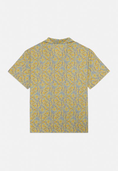 Cămașă cu mânecă scurtă cu model floral galben ornamentat și motive în formă de scroll pe un fundal albastru deschis, văzută din spate.