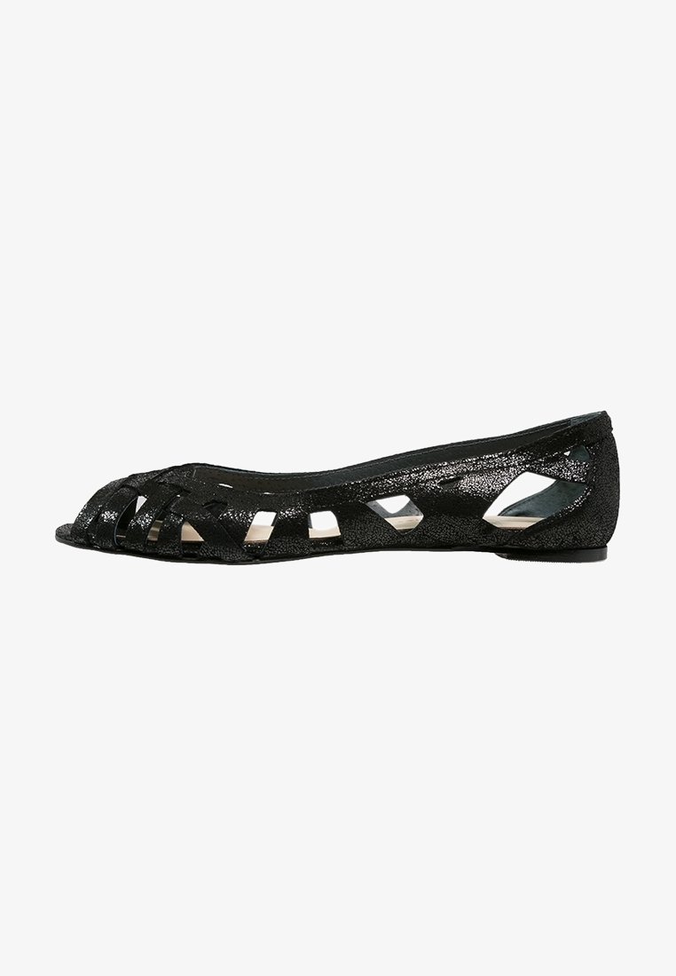 Sandale plate noire avec design à bout ouvert et plusieurs motifs découpés sur les côtés, présentant une finition texturée.