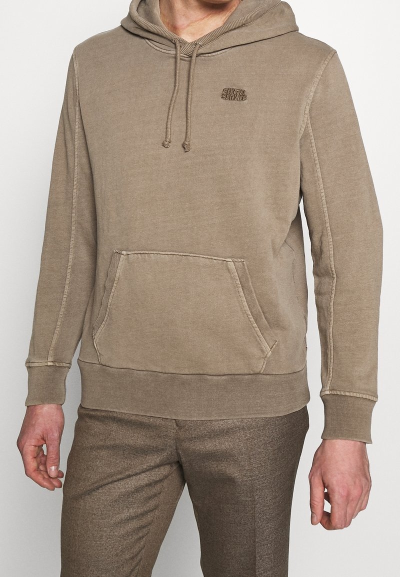 Felpa beige con cappuccio, tasca a marsupio, tessuto testurizzato, polsini a costine e un piccolo logo sul petto. Morbida e con una vestibilità rilassata.