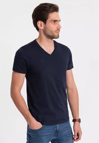 Námořnické tričko s výstřihem do V vyrobené z bavlny, s krátkými rukávy, přiléhavým střihem a hladkou texturou. Nosené s modrými džíny.