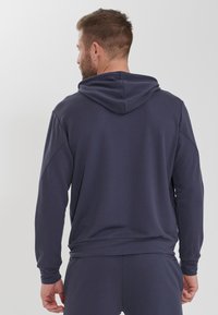 Mörkblå hoodie med avslappnad passform, som har en dragsko i huvan och lång ärm. Mjuk textur och minimalistisk design, inga synliga mönster.
