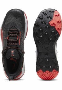 Scarpe sportive con tomaia in rete nera e accenti rossi, suola in gomma spessa con battistrada profondo e dettagli riflettenti sui lacci.