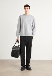 Sudadera gris con un pequeño logo, pantalones negros y una bolsa negra. El conjunto presenta un ajuste relajado y materiales texturizados. Unos zapatos negros completan el look.