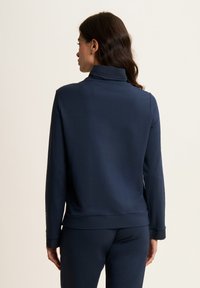 Pullover blu navy a maniche lunghe con colletto alto, realizzato in tessuto morbido. Presenta una vestibilità rilassata e polsini a costine, vista posteriore mostrata.
