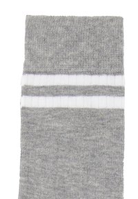 Grå bomuldsstrømpe med ribbet struktur og en kant med to hvide vandrette striber. Stoffet er blødt og en smule fuzzy.