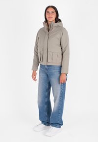 Giacca cropped grigia chiara con cappuccio, dotata di due tasche frontali e una cerniera. Abbinata a jeans blu larghi e sneakers bianche.