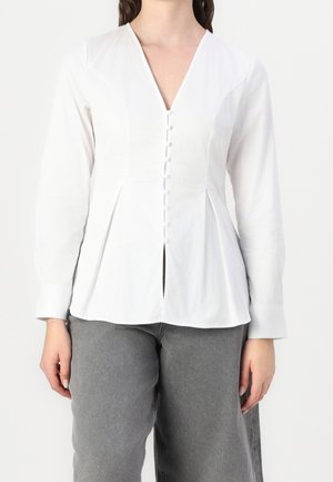 Weiße Bluse mit langen Ärmeln und V-Ausschnitt, mit durchgehender Knopfleiste vorne, Falten-Details und geradem Saum. Kombiniert mit grauen Hosen.