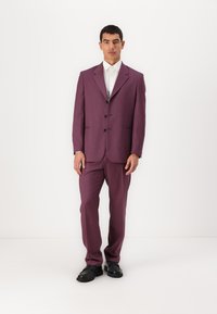 Lila kostym med en texturerad yta, enfärgad jacka med tre svarta knappar och slim fit-byxor. Vit skjorta och svarta skor.