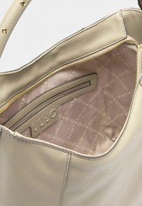 Borsa a tracolla in pelle beige chiaro con una texture morbida. L'interno presenta un rivestimento liscio di un rosa chiaro con un delicato motivo di logo e una tasca con zip.