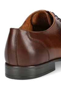 Brązowe skórzane buty wizytowe o gładkiej teksturze, zaokrąglonym obcasie i niskoprofilowej czarnej gumowej podeszwie. Charakteryzują się schludnym przeszyciem i prostym designem.