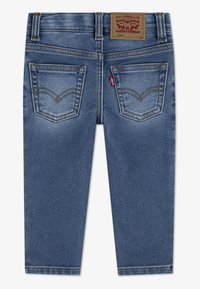 Sötétkék farmerek testhezálló szabással, bőr márkajelzéssel, két varrással díszített hátsó zsebbel és sima textúrával.