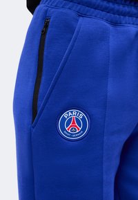 Μπλε αθλητικό παντελόνι με το λογότυπο της Paris Saint-Germain και μαύρη τσέπη με φερμουάρ στο πλάι.