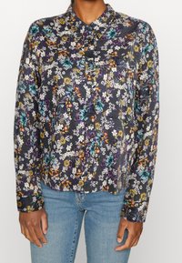 Blommönstrad skjorta i mörknavy med knäppkrage, som har livfulla blommor i blått, gult och vitt på ett lätt tyg.