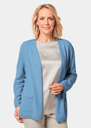 Hellblaues Cardigan aus weichem Stoff, mit offenem Front, langen Ärmeln und zwei vorderen Taschen. Kombiniert mit einem grauen Oberteil.