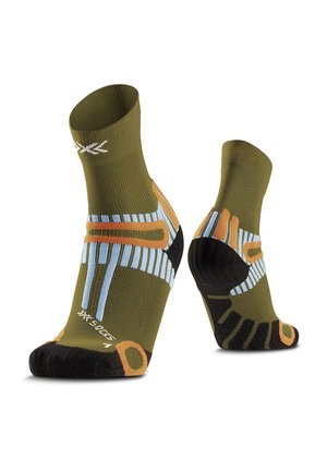 Paire de chaussettes de sport vert olive avec des motifs géométriques noirs, orange et bleus, présentées sur des formes en forme de pied sur fond blanc.